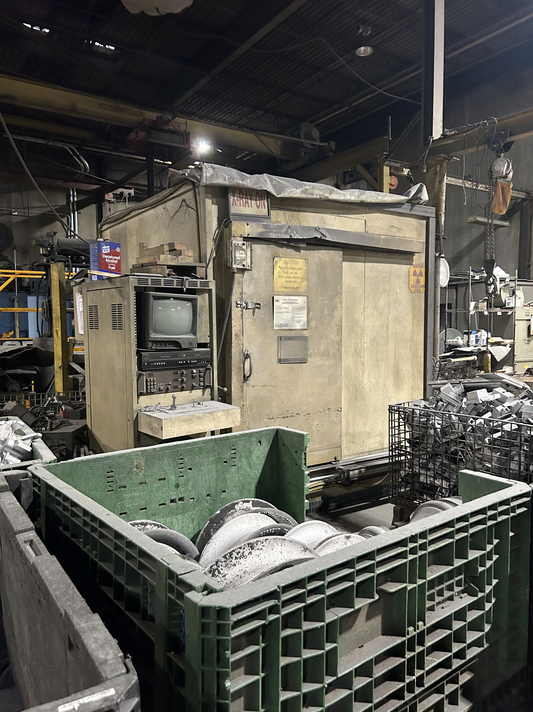 Image of a dusty CRT TV connected to a large square slab of concrete with a metal door. Signs on the side of the concrete read 'X-Ray.' The concrete slab is surrounded by nondescript small pieces of metal in large crates.